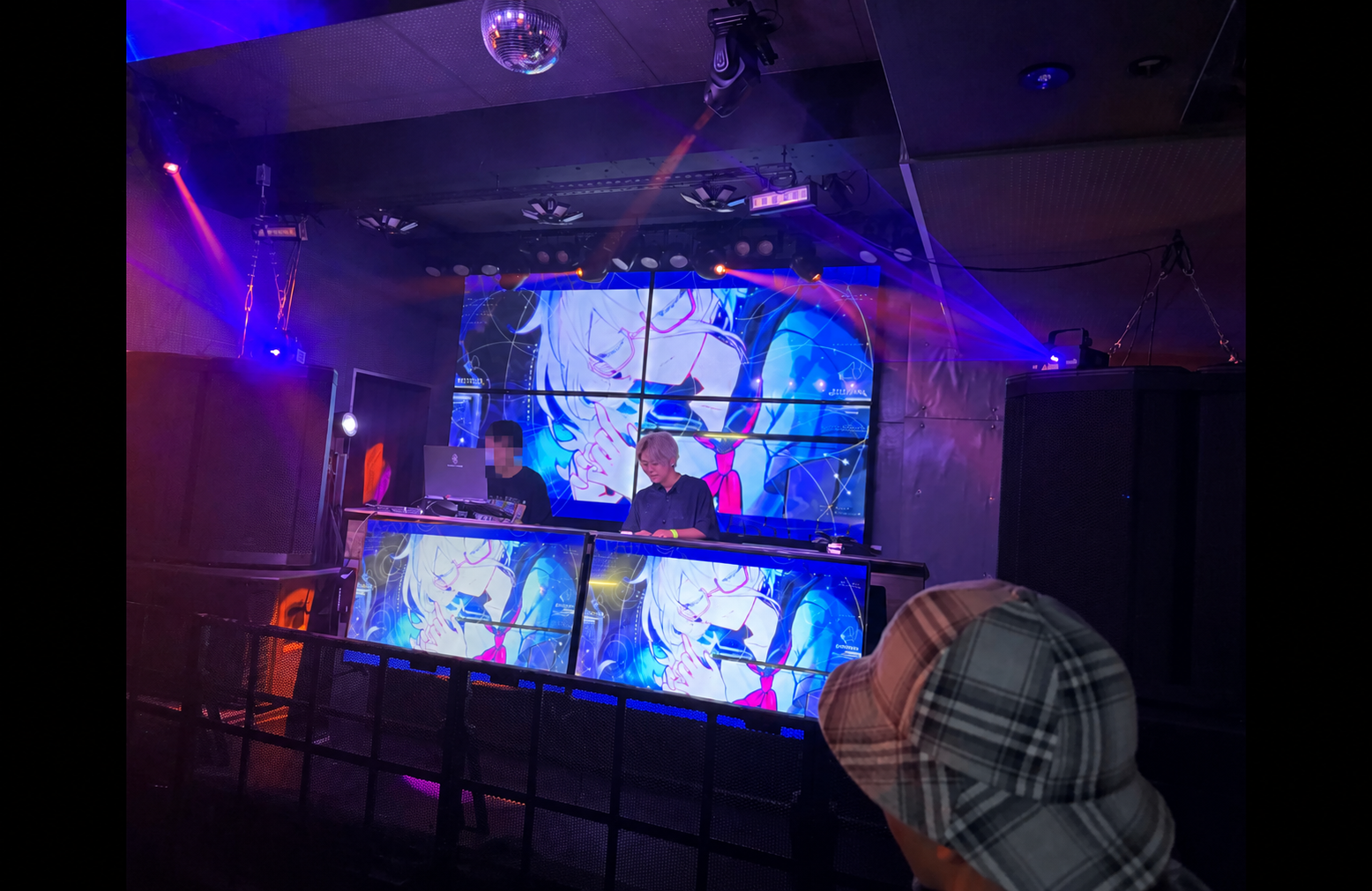 ネオン照明とアニメ映像に囲まれたDJイベントの様子